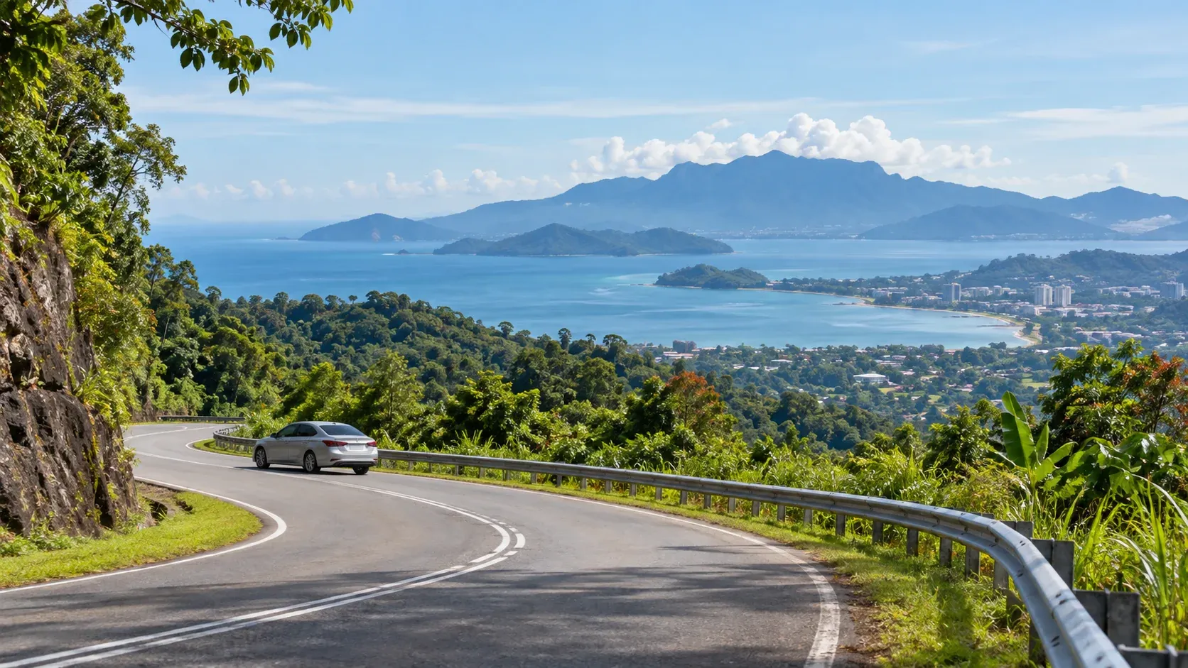 Car driving a winding coastal road in Sabah with a bay, islands and a distant town in view