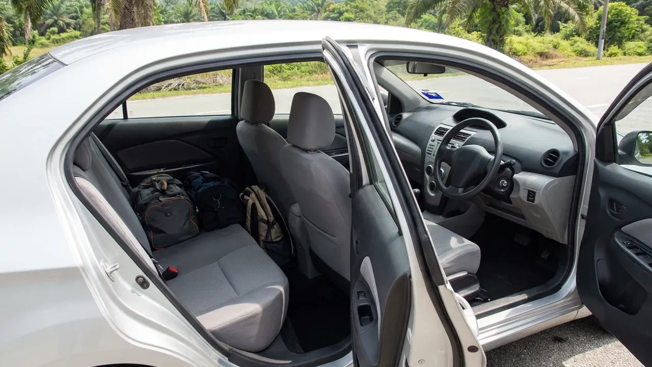 Interior of a silver car seen through the open rear door, with luggage space visible in the back.
