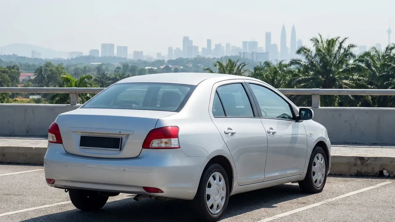 Rear view of an unbranded silver car parked at a Malaysian highway rest area with a distant city skyline.