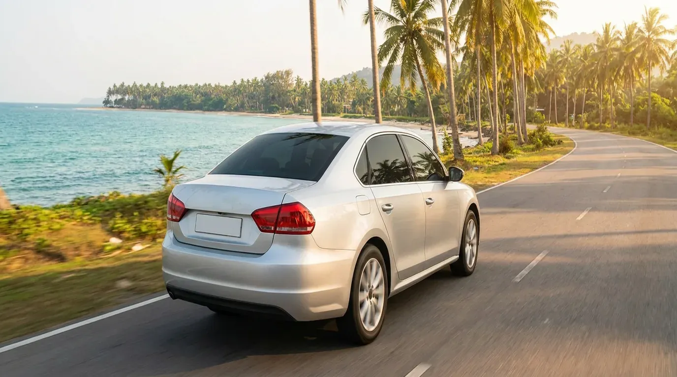 Kereta sewaan memandu di sepanjang jalan pantai Penang dengan pohon kelapa dan laut di sebelah.
