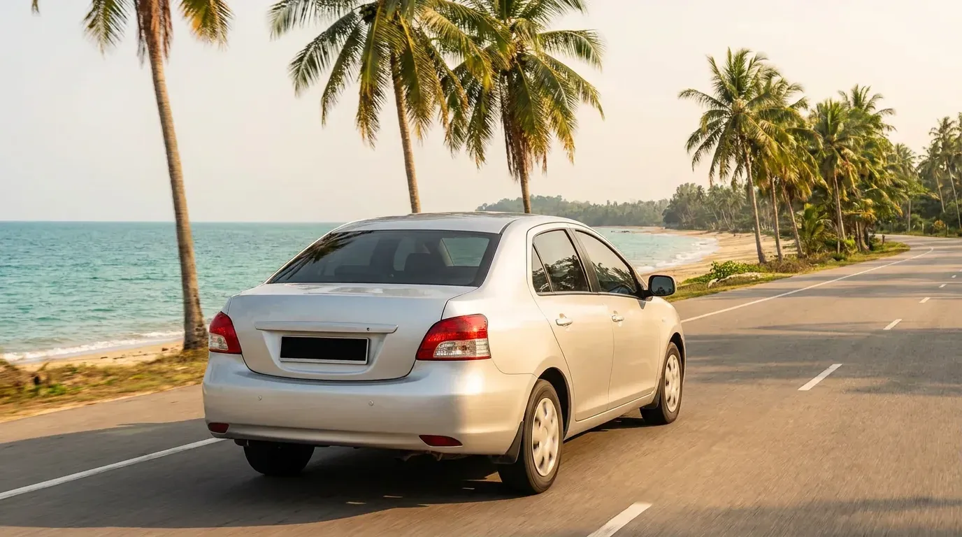 Kereta sewaan memandu di sepanjang jalan pantai Penang dengan pohon kelapa dan laut di sebelah.