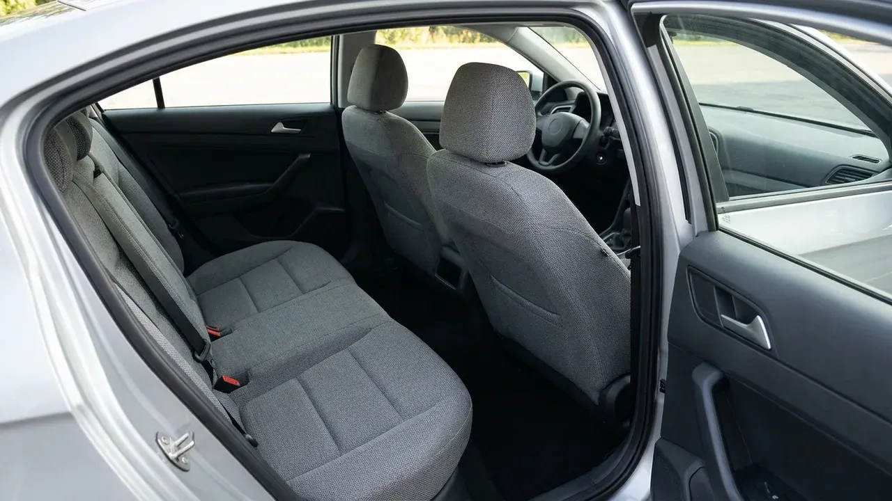 Tidy cabin of a modern sedan with grey fabric seats and a roomy back seat, seen through the open rear passenger door.