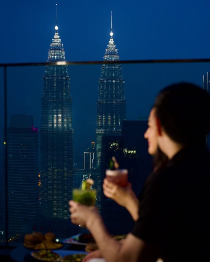 Two people enjoying drinks with Petronas Towers in background at Vertigo, one of the best rooftop bars in KL